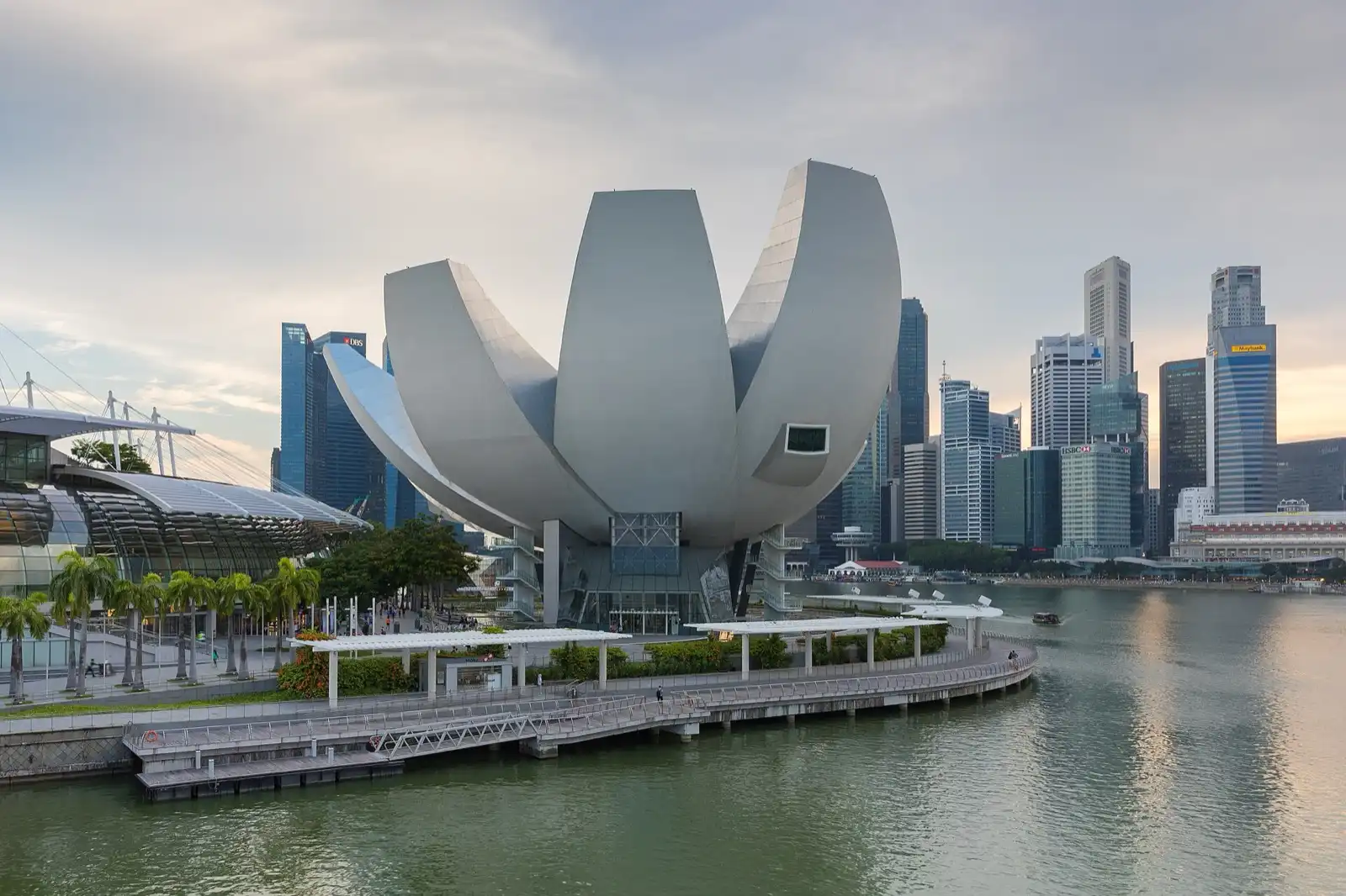 A white lotus-shaped building on the waterfront, with the city's towers behind it.