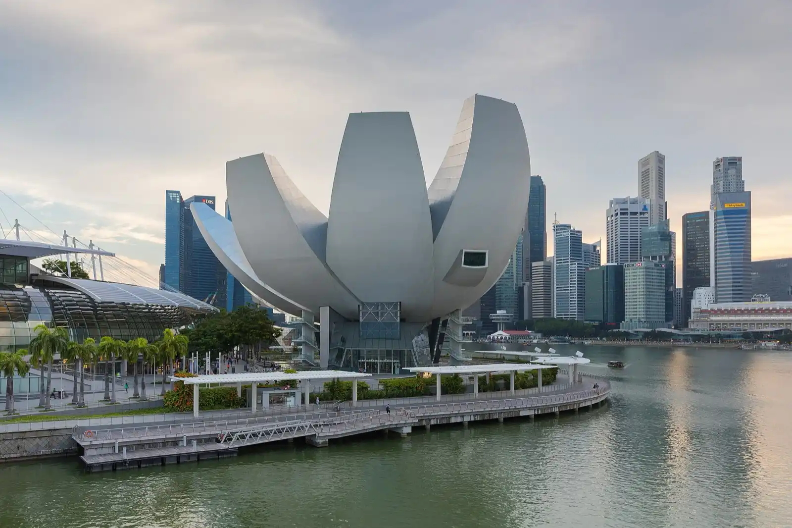 A white lotus-shaped building on the waterfront, with the city's towers behind it.