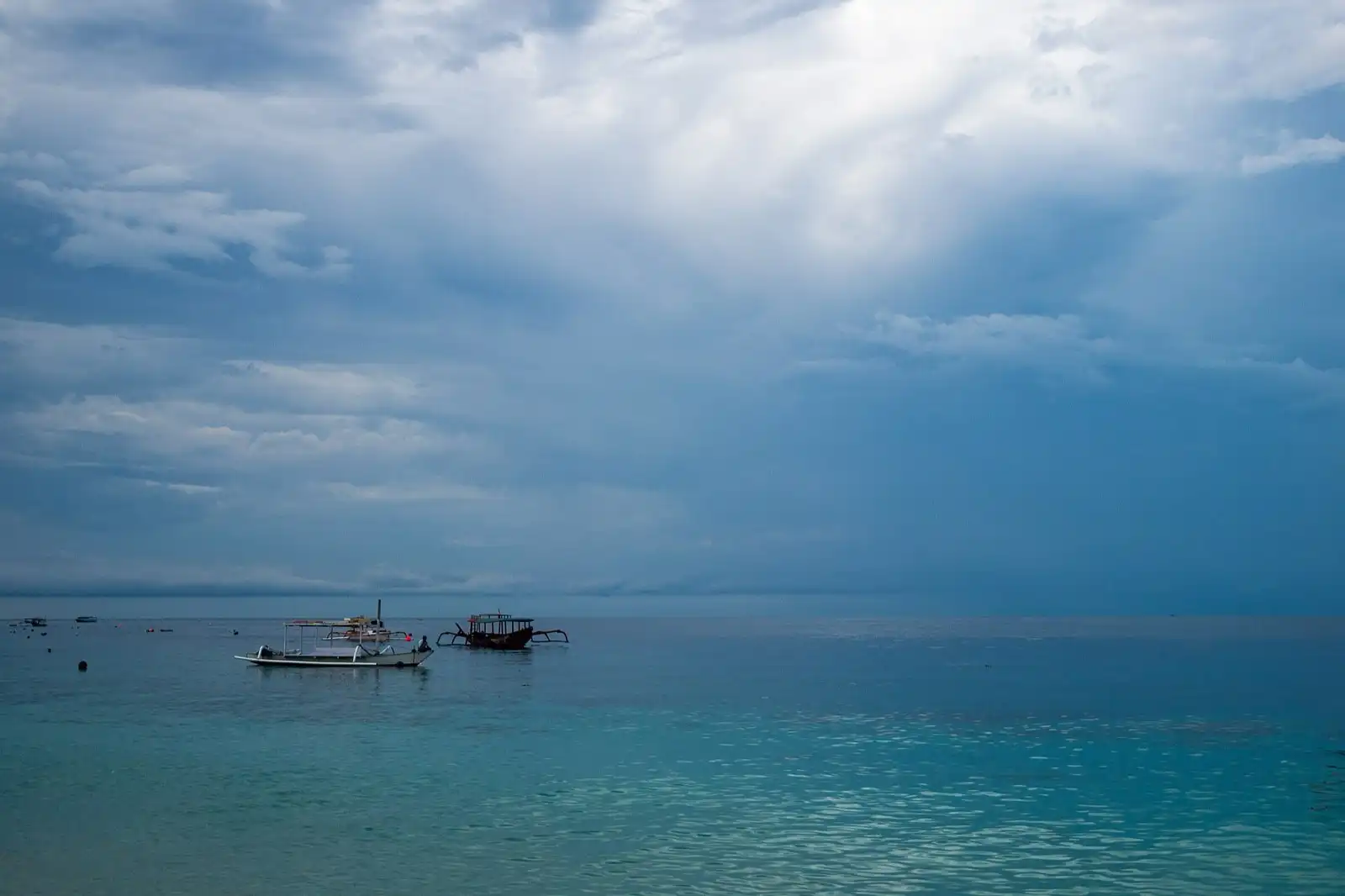 Two small outrigger boats on calm open sea under heavy cloud.
