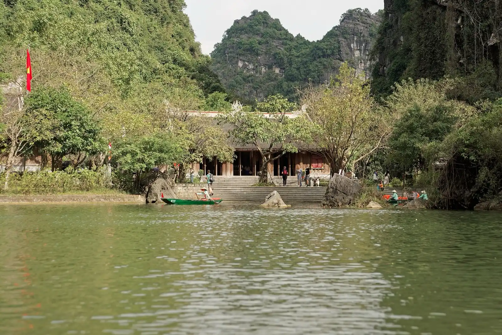 A small boat on a green river between steep limestone hills, with a temple on the bank.