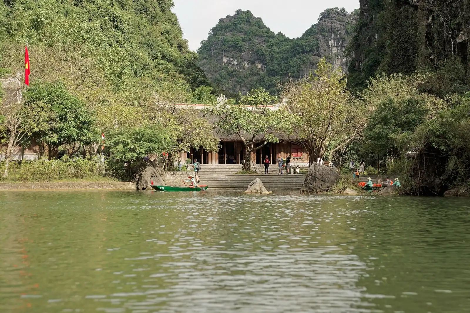 A small boat on a green river between steep limestone hills, with a temple on the bank.